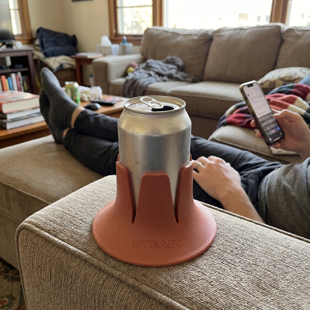 A can standing in a terracotta Steadi on the cushion beside someone reclined with their feet up.